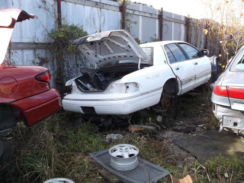 1999 Mercury Grand Marquis - A white sedan with its trunk open is parked next to a red car with its trunk open. A silver sedan is partially visible to the right.