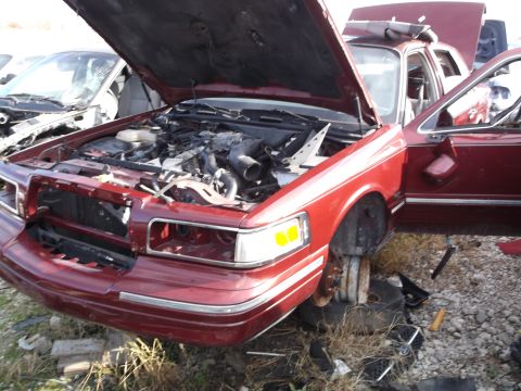 1999 Mercury Grand Marquis - The front passenger side of a dark red sedan is shown with the hood and driver's side door open, revealing the engine compartment. The vehi…