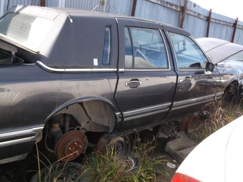 1999 Mercury Grand Marquis - The side view of a dark gray sedan, possibly a Lincoln Town Car, shows its rear wheel well with exposed rusty brake components. The vehicle…