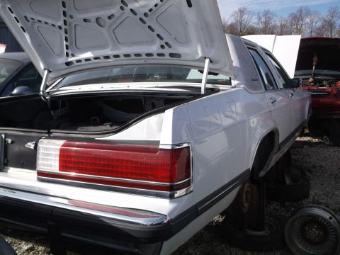 1999 Mercury Grand Marquis - The rear passenger side of a white sedan is shown with the trunk open, revealing the interior. A red car with its hood open is visible in t…
