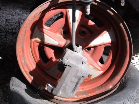 1999 Mercury Grand Marquis - A close-up view of a red five-spoke wheel with a gray brake caliper attached. The wheel is mounted on a flat tire, and the background consi…