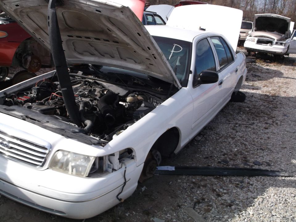 White sedan with hood open in a junkyard, engine visible.