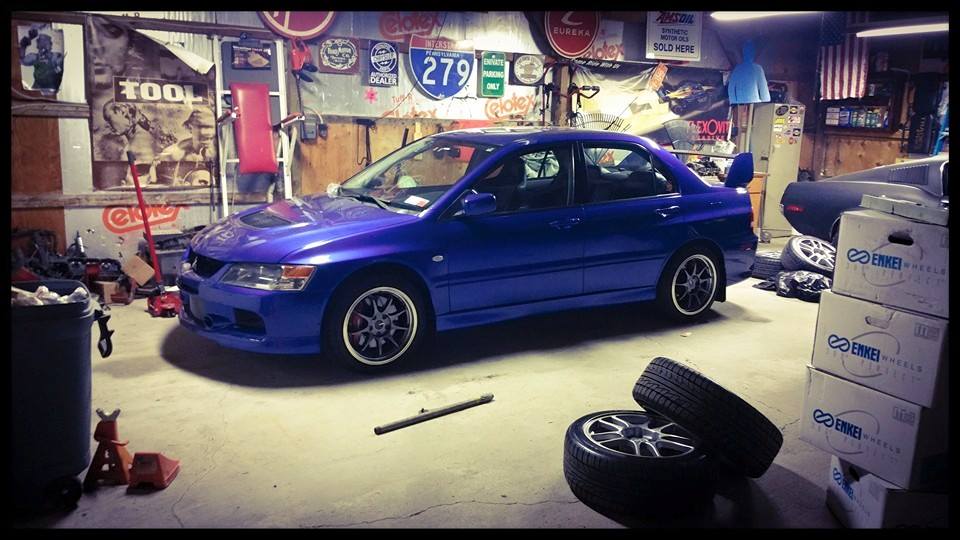 Blue Mitsubishi Lancer Evolution sedan in a garage with Enkei wheel boxes and tires.