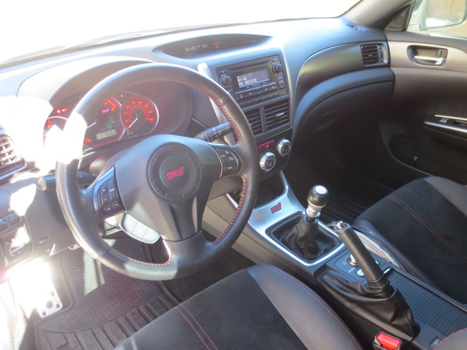 Interior of a Subaru WRX STI, showing steering wheel, dashboard, and manual shifter.