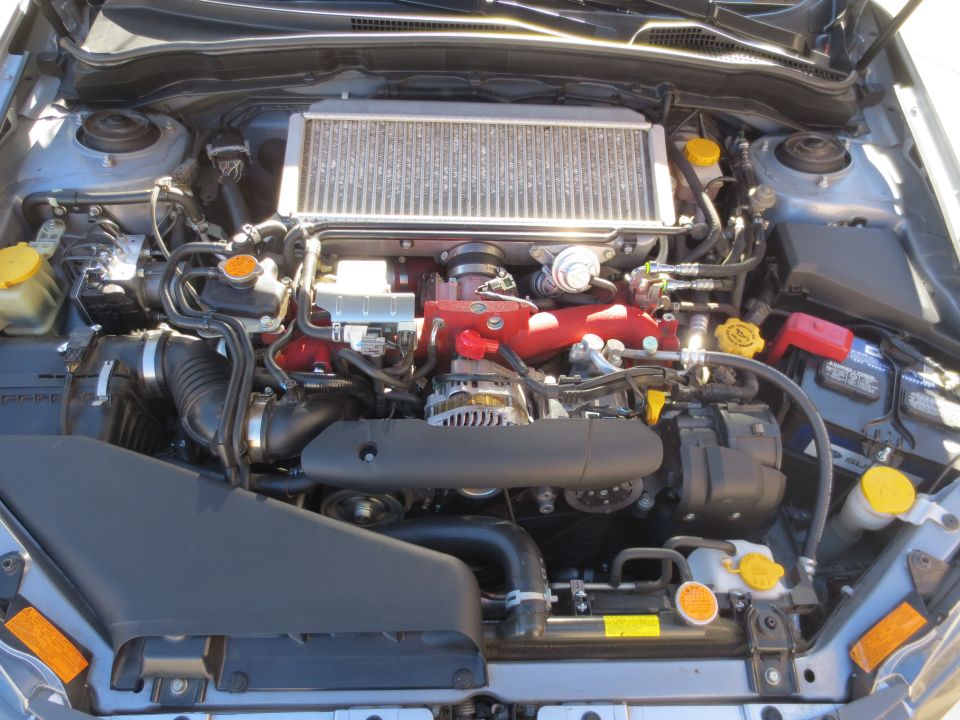 Close-up of a Subaru WRX STI engine bay with intercooler and red intake manifold.