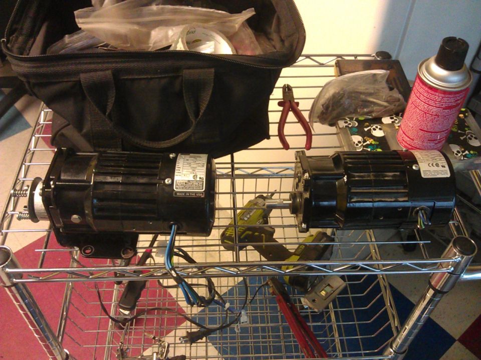 Two black electric motors on a shelf with tools and a spray can.