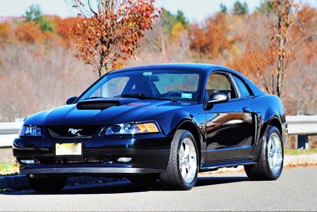 Black 2002 Ford Mustang coupe with custom wheels parked outdoors in autumn.