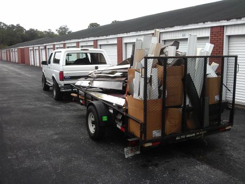1994 Ford Bronco - A white 1990s Ford Bronco is parked next to a utility trailer loaded with construction debris, including cardboard boxes and metal pieces.…