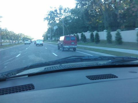 1994 Ford Bronco - A red Ford Econoline van is driving on a highway with other vehicles. The photo is taken from the perspective of the driver's seat, showing…