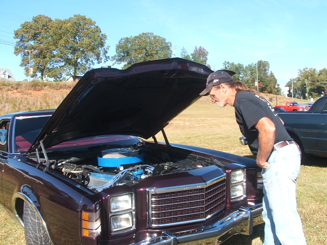 Man looking at the engine of a dark purple classic car with hood open.