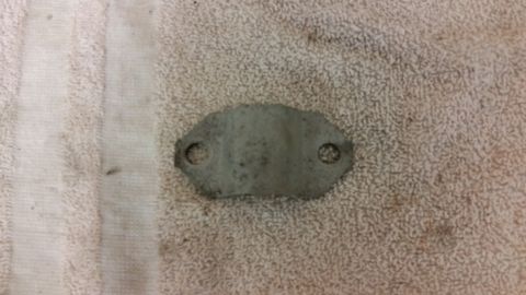2015 Chevrolet new - A metal bracket with two holes is shown on a textured fabric surface. The bracket appears to be a vehicle part.