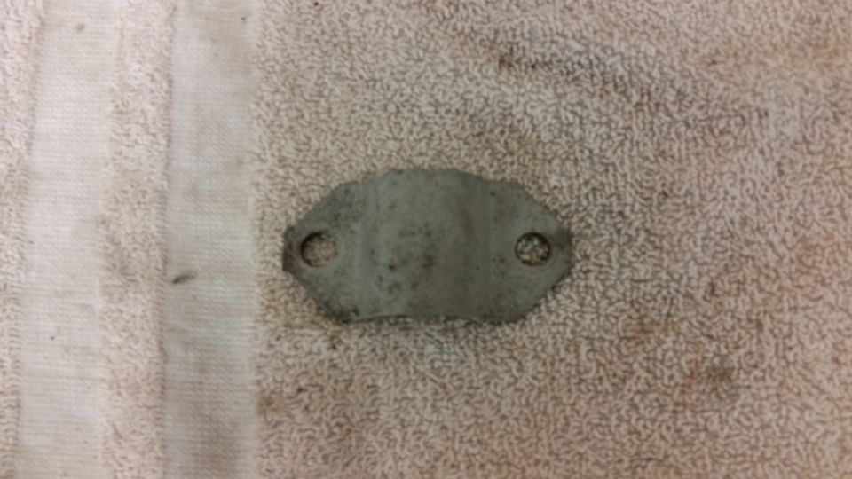 Metal bracket with two holes on a textured fabric surface.