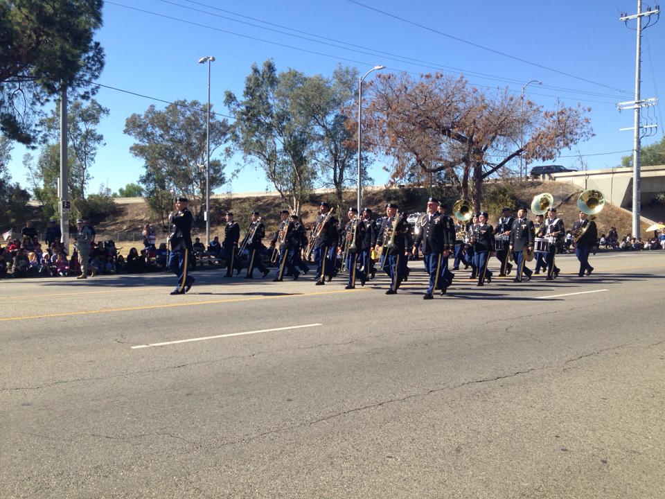 A marching band parades down a street with spectators on the side.