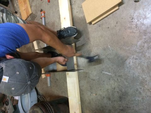 1979 Ford Bronco - A person wearing blue shorts and a grey baseball cap is working on a piece of metal with a hammer. They are using clamps and wooden beams a…
