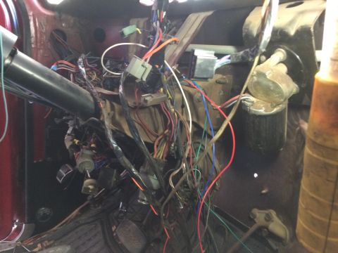 1979 Ford Bronco - The interior of a vehicle shows a complex and messy wiring harness under the dashboard, with various connectors and cables visible. A steer…