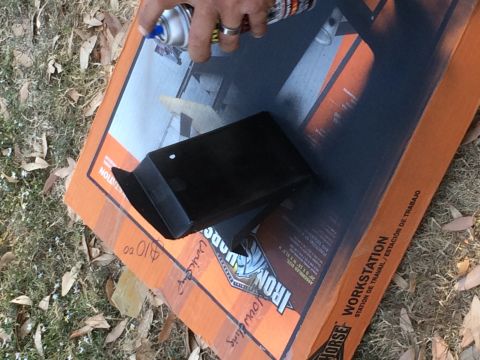 1979 Ford Bronco - A person is spray painting a black object on top of an orange and black cardboard box that says "Iron Horse Workstation". The box is on the…