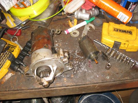 1994 Ford Bronco - Two starter motors and a yellow DeWalt tool case are on a workbench with various tools and supplies.