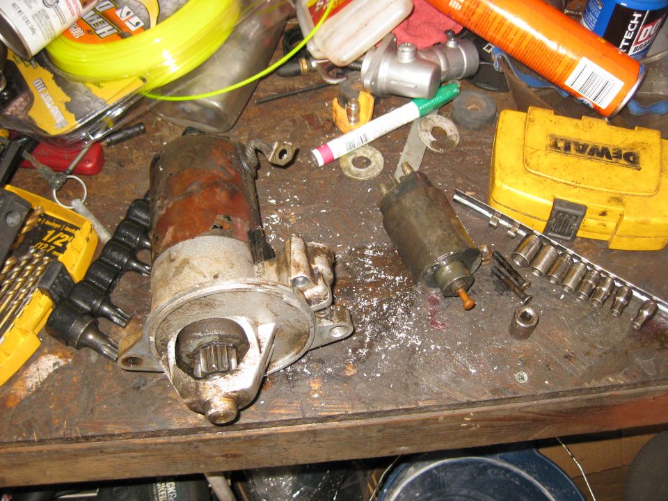 Two starter motors and a yellow DeWalt tool case on a workbench with tools.