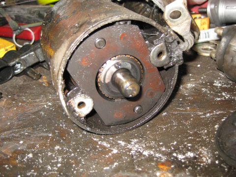 1994 Ford Bronco - A close-up view of a heavily used and dirty starter motor assembly, likely from a 1994 Ford Bronco, resting on a cluttered workbench.