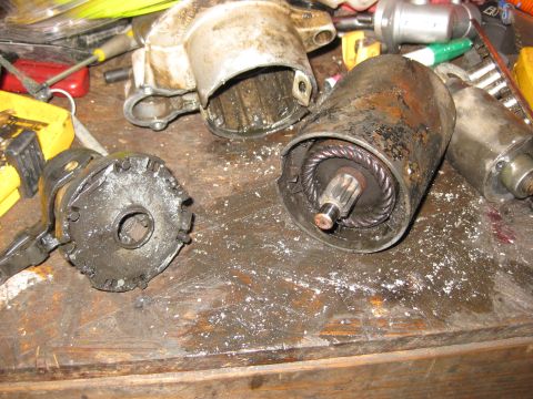 1994 Ford Bronco - Two disassembled parts of a starter motor are on a wooden workbench covered in dust and debris. The parts appear to be heavily used and pos…