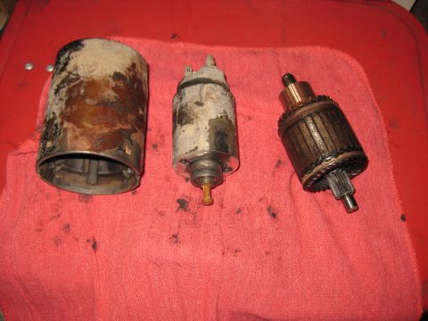1994 Ford Bronco - Three disassembled parts of a starter motor are laid out on a red cloth. The parts appear dirty and used, with visible rust and grime.