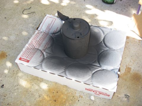 1994 Ford Bronco - A gray cylindrical object, possibly a filter or canister, sits on a cardboard box with a textured surface. The box has text that reads "ROY…