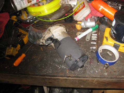 1994 Ford Bronco - A disassembled starter motor assembly is shown on a cluttered workbench with various tools and automotive fluids.