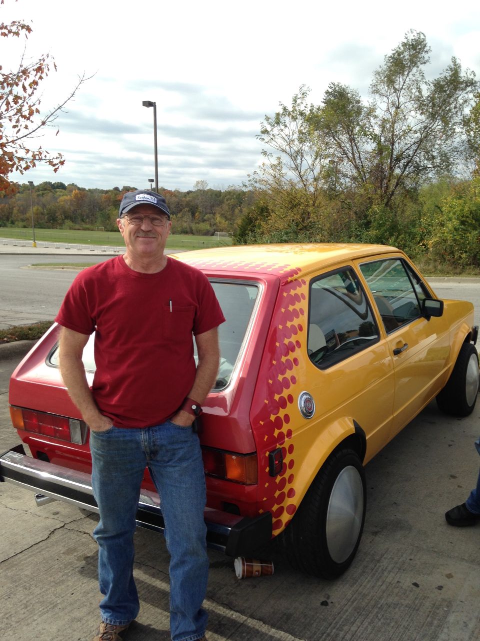 Man standing next to a red and yellow Volkswagen Rabbit.