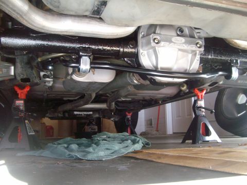 2004 Ford Crown Victoria - The underside of a Ford Crown Victoria is shown, supported by jack stands. A Ford Racing differential cover and a sway bar are visible, alo…