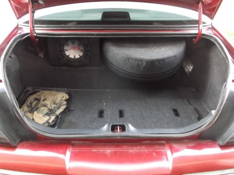 1999 Mercury Grand Marquis - Open carpeted trunk of a maroon sedan containing a subwoofer enclosure, spare tire and a folded tarp.