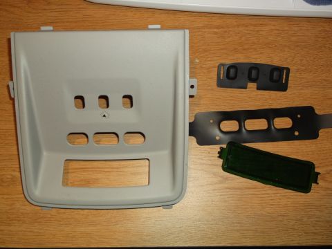 1999 Mercury Grand Marquis - A light gray plastic interior trim piece with multiple cutouts is laid out on a wooden surface next to several black rubber gaskets and a d…