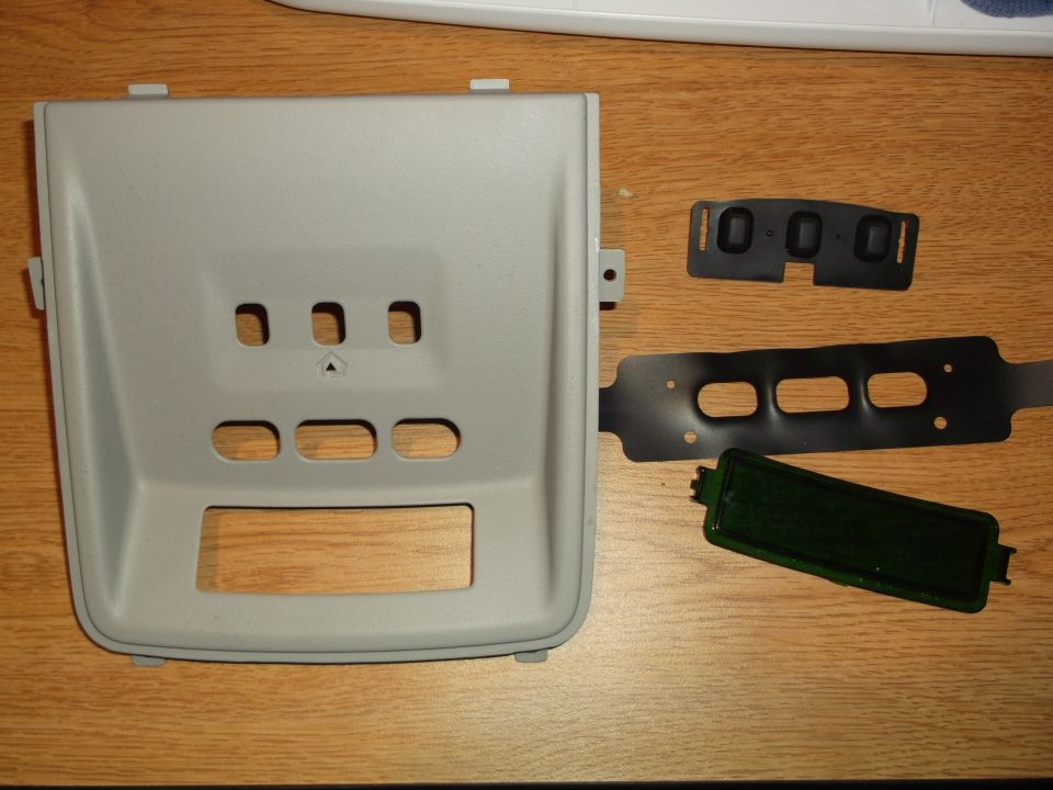 Light gray plastic interior trim piece with cutouts, black rubber gaskets, and a dark green object on a wooden surface.
