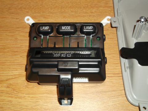 1999 Mercury Grand Marquis - A black automotive interior control panel with three buttons labeled LAMP, MODE, and LAMP is shown on a wooden surface next to a gray plast…