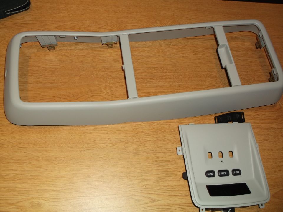 Gray automotive interior trim bezel and control panel with buttons on a wooden surface.