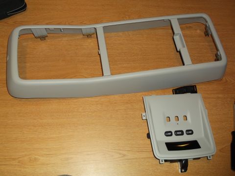 1999 Mercury Grand Marquis - A light gray trim piece with multiple openings and mounting brackets sits above a separate gray console panel with three buttons labeled "L…