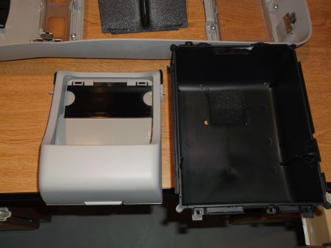 1999 Mercury Grand Marquis - Two disassembled parts of a center console storage compartment are shown on a wooden surface. The left part is a light gray plastic bin wit…