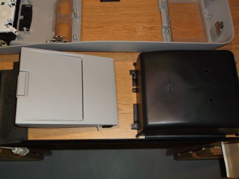 1999 Mercury Grand Marquis - Two automotive interior parts are laid out on a wooden surface. On the left is a light gray storage compartment with a hinged lid, and on t…