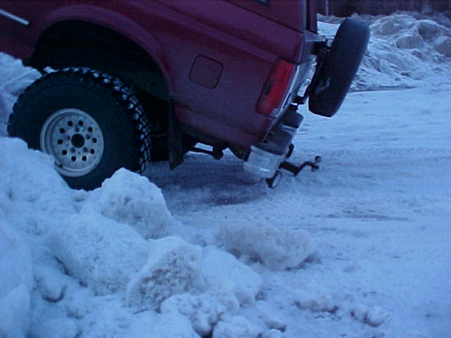 Close rear quarter of red Ford Bronco on large tire with exhaust tip and spare carrier over snow