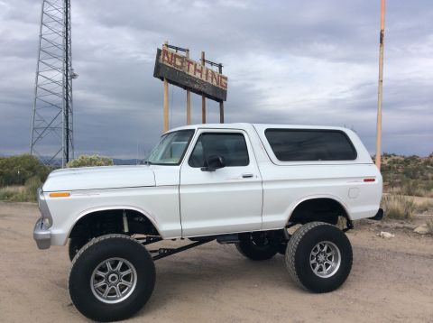 1979 Ford Bronco - A lifted white 1979 Ford Bronco is parked on a dirt road in a desert landscape, with a weathered sign that reads "NOTHING" in the backgroun…