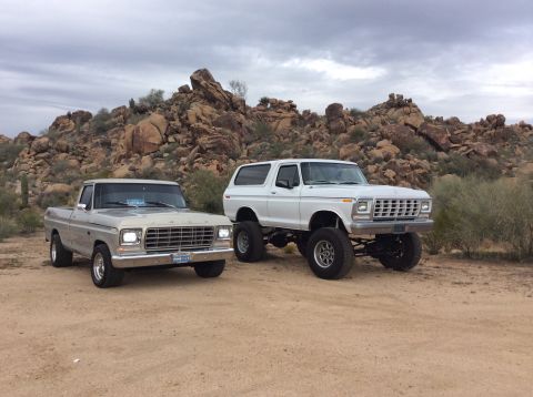 1979 Ford Bronco - A lifted white 1979 Ford Bronco is parked next to a silver 1979 Ford pickup truck in a desert landscape with rocky hills in the background.