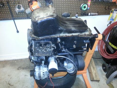 1994 Ford Bronco - A black engine block is mounted on an orange engine stand, with an alternator and oil filter visible. Various tools and an air compressor a…