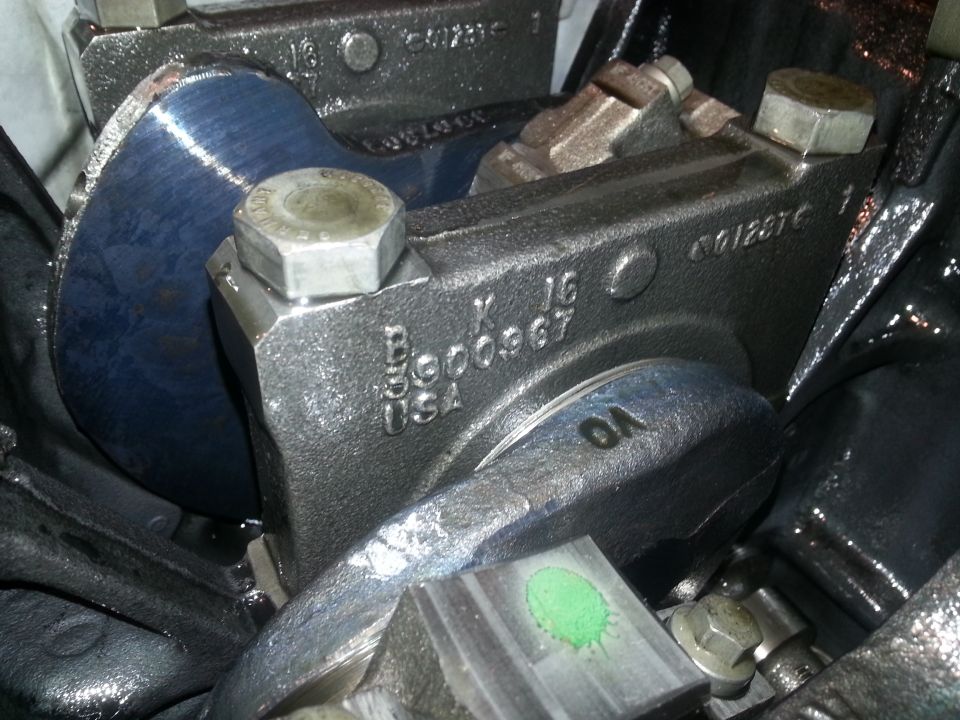 Cast iron engine part with markings 'B 6000967 K 16 USA' and '6012876', and a blue metal surface.
