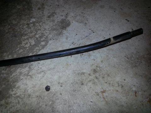 1994 Ford Bronco - A black, curved hose or cable lies on a concrete floor. A small, dark, circular object is visible on the floor near the hose.