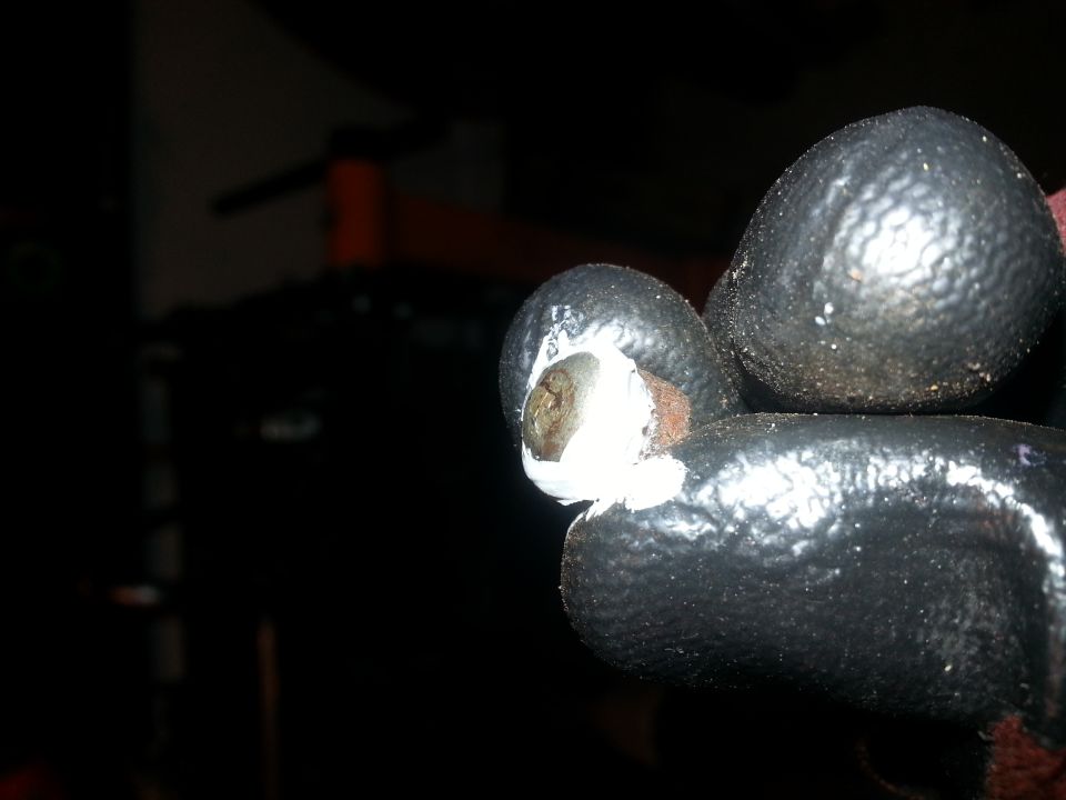 Close-up of a gloved hand holding a bolt with white sealant.