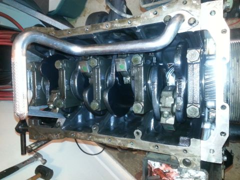 1994 Ford Bronco - A partially assembled engine block is shown, with the crankshaft and connecting rods visible. A metal oil pan gasket is attached to the bot…