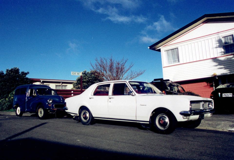 White sedan and blue van parked on street with Adair Way sign.