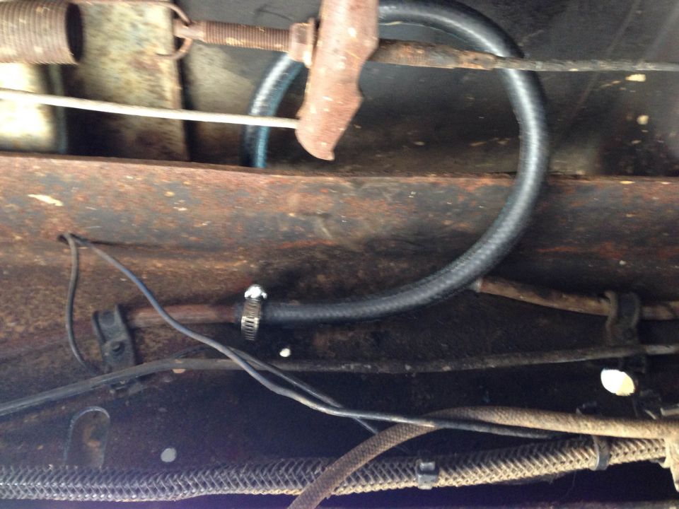Black fuel hose with hose clamp routed in a loop under vehicle chassis near rusty metal and wiring.
