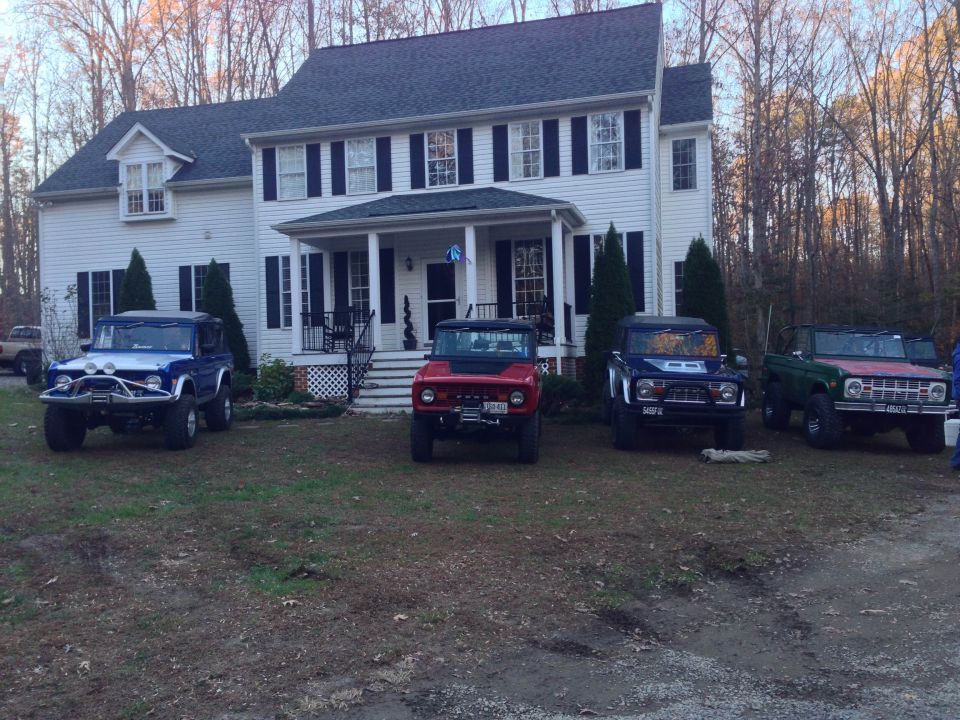 Four Ford Broncos parked in front of a white house.