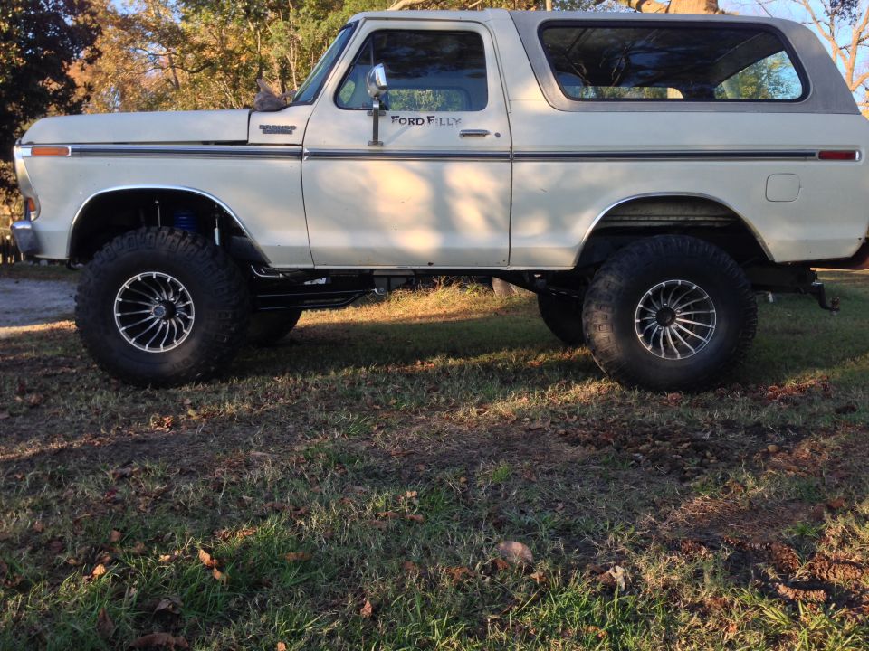 Side view of a lifted cream-colored 1970s Ford Bronco with off-road tires and custom rims.