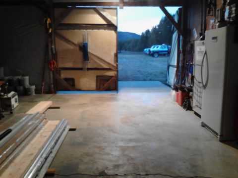 1989 Ford Bronco - The interior of a garage shows a large open doorway revealing two vehicles parked outside in a rural setting. To the right, a white refrige…